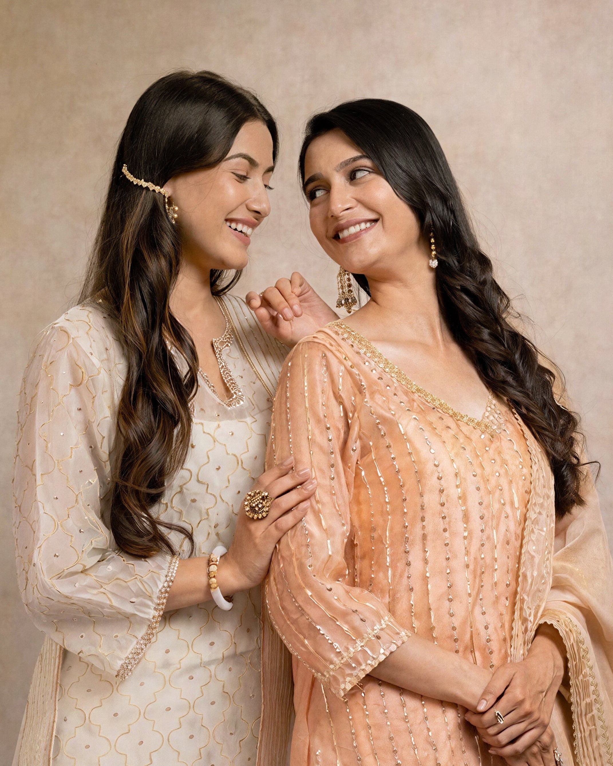 Two women in traditional attire standing close together against a neutral background