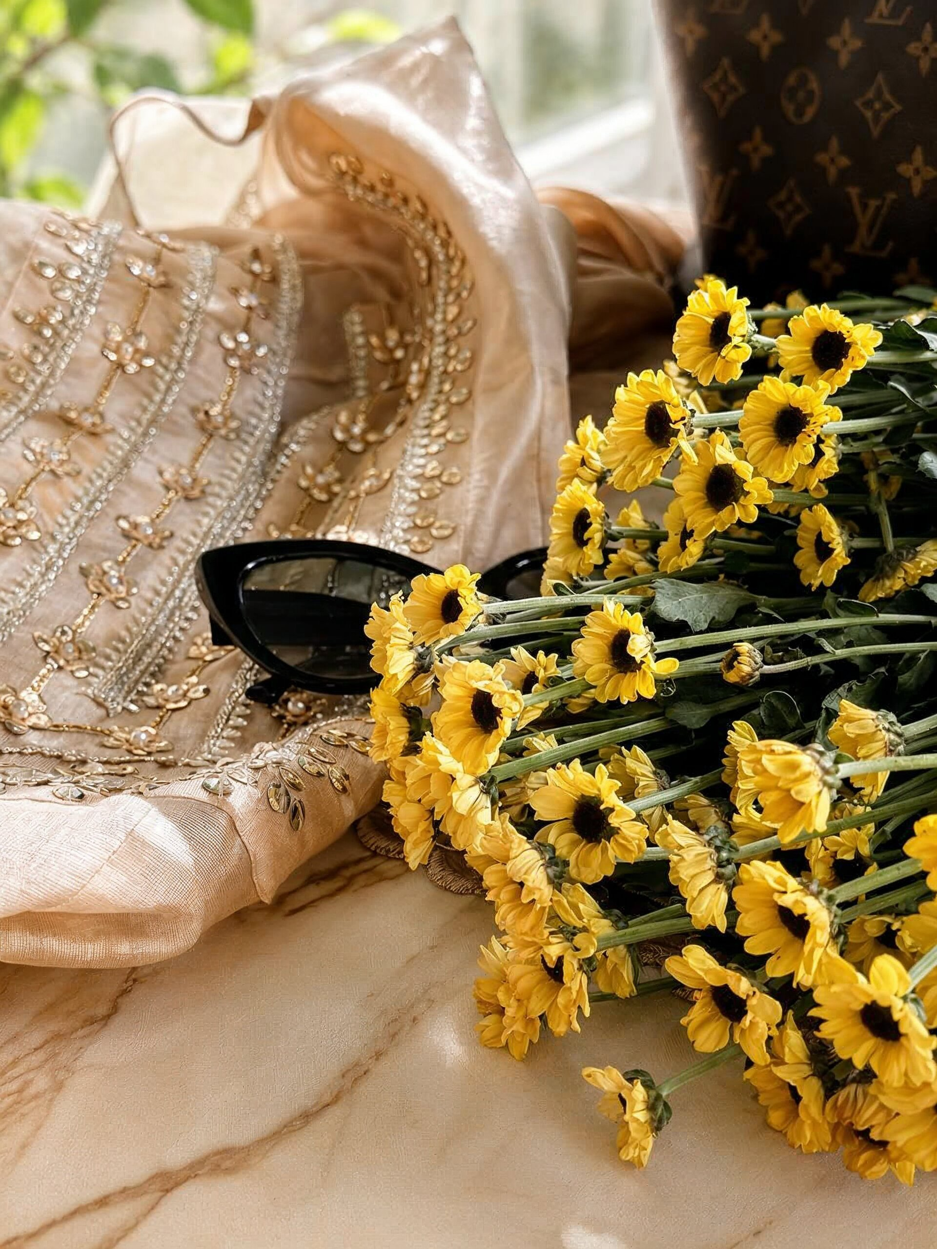 Bouquet of yellow flowers on a marble surface with a decorative headscarf and sunglasses.