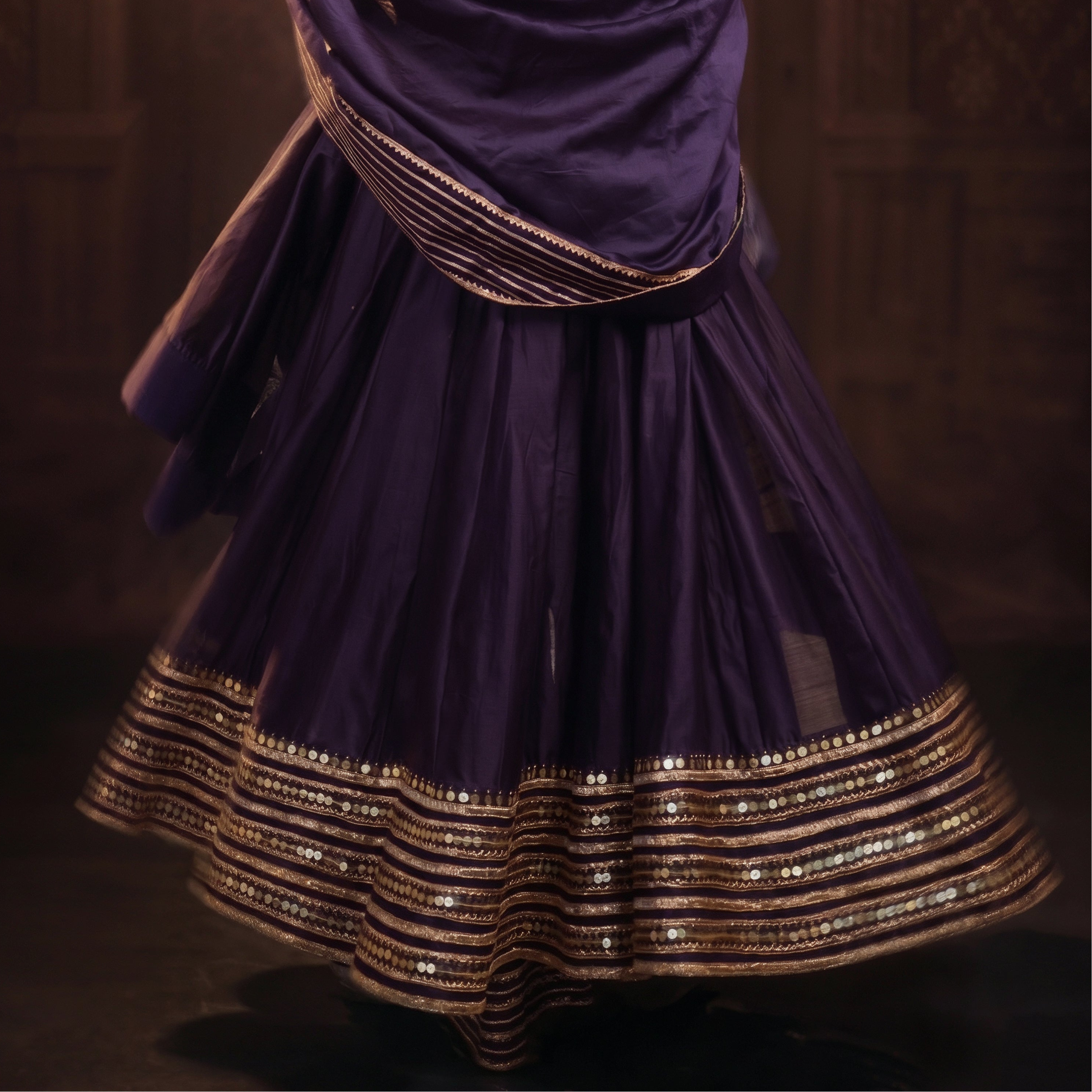 Person wearing a purple traditional outfit with gold accents in a dark setting